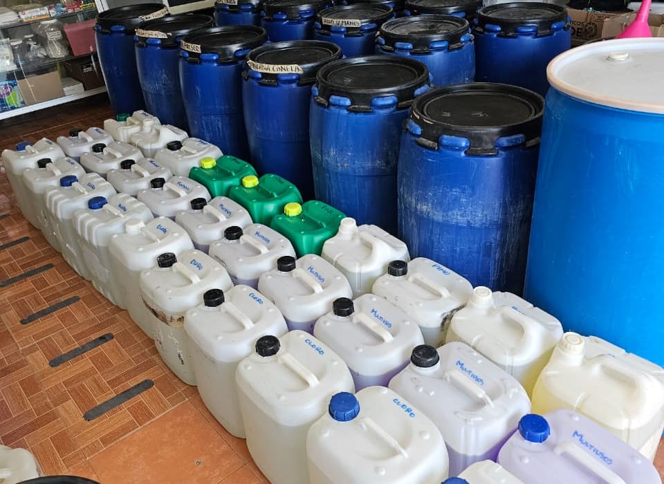 Filas de garrafas de 20 litros rotuladas a mano —cloro, multiusos y pino— junto a tambos azules en la tienda de San José del Cabo.